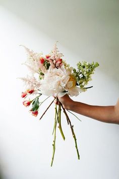 a person holding a bouquet of flowers in their hand with white wall and background behind them