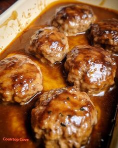 meatballs covered in gravy sitting on top of a baking pan filled with sauce
