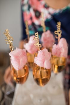 three champagne flutes with pink flowers in them on a table next to a woman's hand