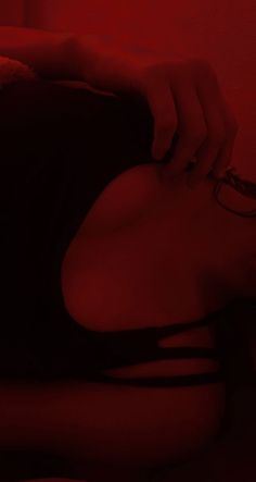a woman wearing glasses laying on top of a bed next to a red light in the dark