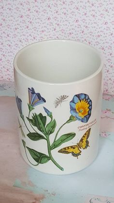 a white cup with blue and yellow butterflies painted on the side, sitting on a table