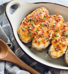 baked potatoes topped with bacon and cheese in a white casserole dish next to a wooden spoon