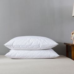 two pillows sitting on top of a bed next to a night stand with a lamp