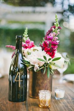 two vases filled with flowers on top of a wooden table next to a wine bottle