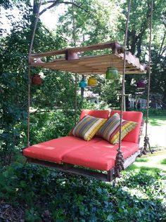 a swing bed in the middle of some bushes and trees with pillows on top of it