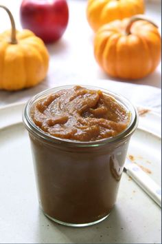 a glass jar filled with peanut butter sitting on top of a white plate next to pumpkins
