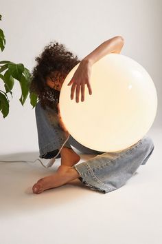 a woman sitting on the floor holding an illuminated balloon in front of her face with both hands