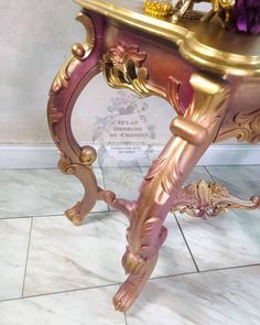 an ornate gold and pink table with flowers on it's top, next to a white marble floor