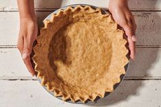 two hands holding a pie crust on top of a white table