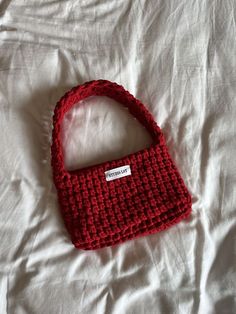 a crocheted red purse sitting on top of a white bed covered in sheets