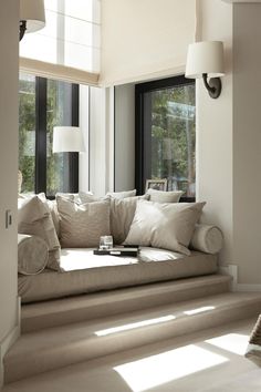 a living room filled with lots of white furniture and pillows on top of a window sill