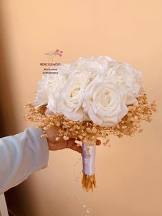 a bouquet of white roses being held by a person's hand in front of a wall