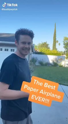 a man holding up a sign that says the best paper airplane ever in front of his house