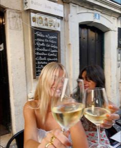 two women sitting at an outdoor table with wine glasses