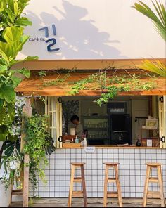 the outside of a cafe with three stools in front of it and plants growing on the wall