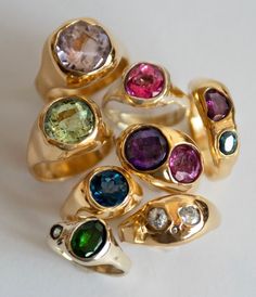 five different colored stones in gold rings on a white surface, with one ring facing the camera