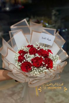 a bouquet of red roses and baby's breath is held by someone in arabic
