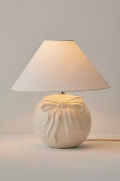 a white table lamp with a bow on the top and a light shade over it