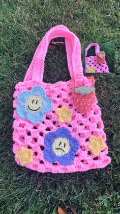 a pink crocheted bag sitting on top of a green grass covered field next to a toy