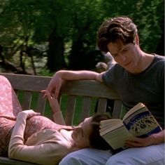 a woman laying on top of a wooden bench next to a man reading a book