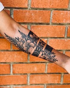 a person's arm with flowers on it and a brick wall in the background