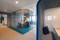 two people are sitting at a table in an office with glass walls and blue carpet