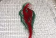 a red piece of yarn sitting on top of a white cloth covered in green thread