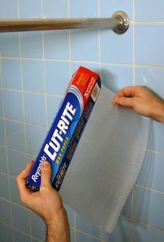 a person holding a tube of toilet paper in front of a blue tiled bathroom wall
