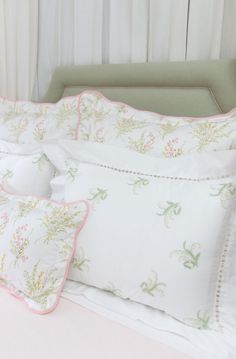 a bed with white sheets and pink trimmings on the headboard, along with two pillows