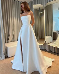 a woman standing in front of a mirror wearing a white wedding dress with high slit