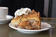 a slice of apple pie on a plate with a fork and cup of coffee in the background