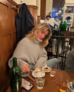 a woman sitting at a table with two cups of coffee in front of her and some drinks on the side