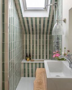 a small bathroom with green and white tiles on the walls, a skylight above the bathtub