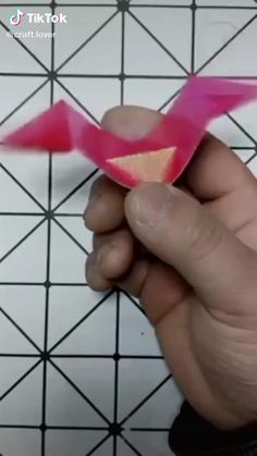 someone is cutting out an origami bird with pink and red paper on it