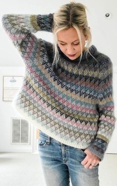 a woman is wearing a multicolored sweater and looking down at her hand on her head
