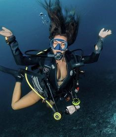 a woman scubas in the water with her hands up and wearing a diving mask