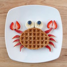 a plate topped with waffles and fruit on top of a wooden table in the shape of a crab