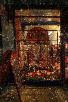 a store front with christmas decorations on display in the window and snow falling around it