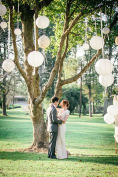 a bride and groom standing in front of a tree with paper lanterns hanging from it