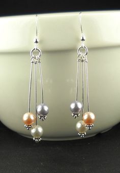two different colored pearls are hanging from silver earwires on a white bowl with a black background