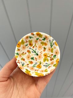 a hand holding a paper plate with flowers painted on the outside and yellow around it