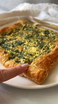 a piece of quiche with spinach and cheese being held by a person's finger