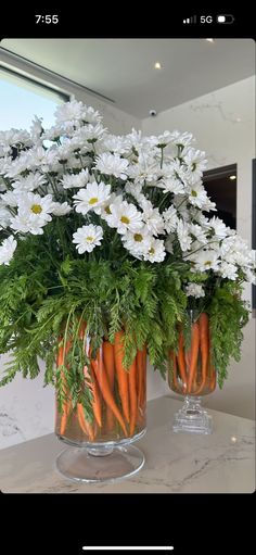 some carrots and daisies in a glass vase on a counter with white flowers