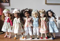 a group of dolls standing next to each other on top of a wooden table in front of a wall