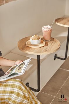 a person sitting at a table with food and drink on it while reading a magazine