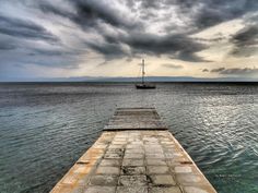 a boat floating on top of the ocean next to a pier under a cloudy sky