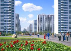 many people are walking around in front of some tall buildings with red flowers on the ground