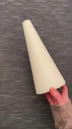 a hand holding a white cone on top of a gray surface with the tip pointing towards it