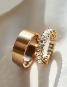two gold wedding rings sitting on top of a white sheet with the light shining through them