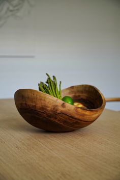 a wooden bowl filled with green vegetables on top of a table